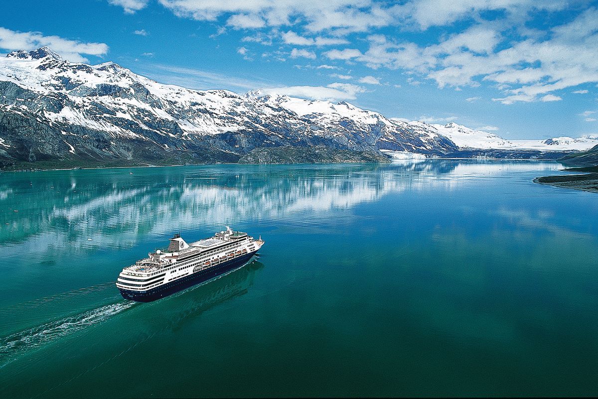Cruise ship sailing on turquoise water, snow-capped mountains in background. Sunny day.