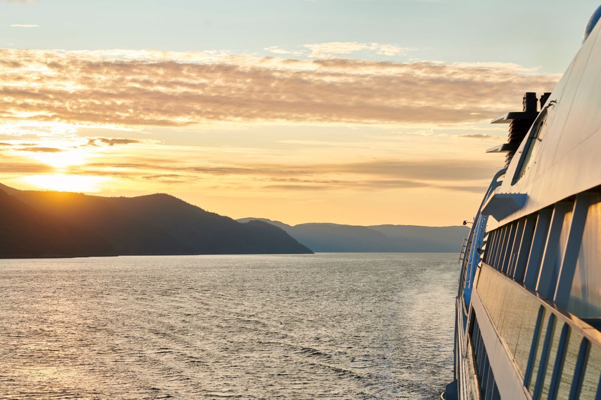 A view from the deck of a ferry during a golden sunset over calm water with hills in the distance.