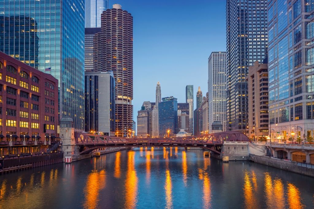 Chicago River at dusk, surrounded by skyscrapers, reflecting lights on the water.