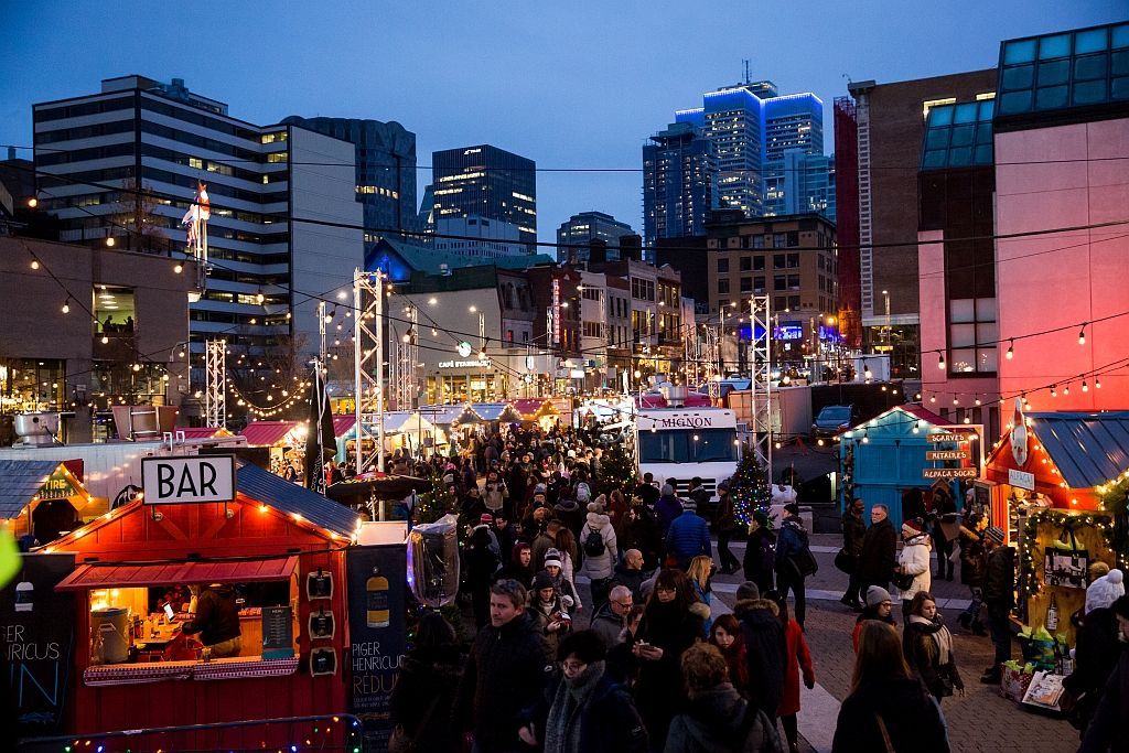 Crowded evening street market with colourful food stalls and city skyline lights in the background