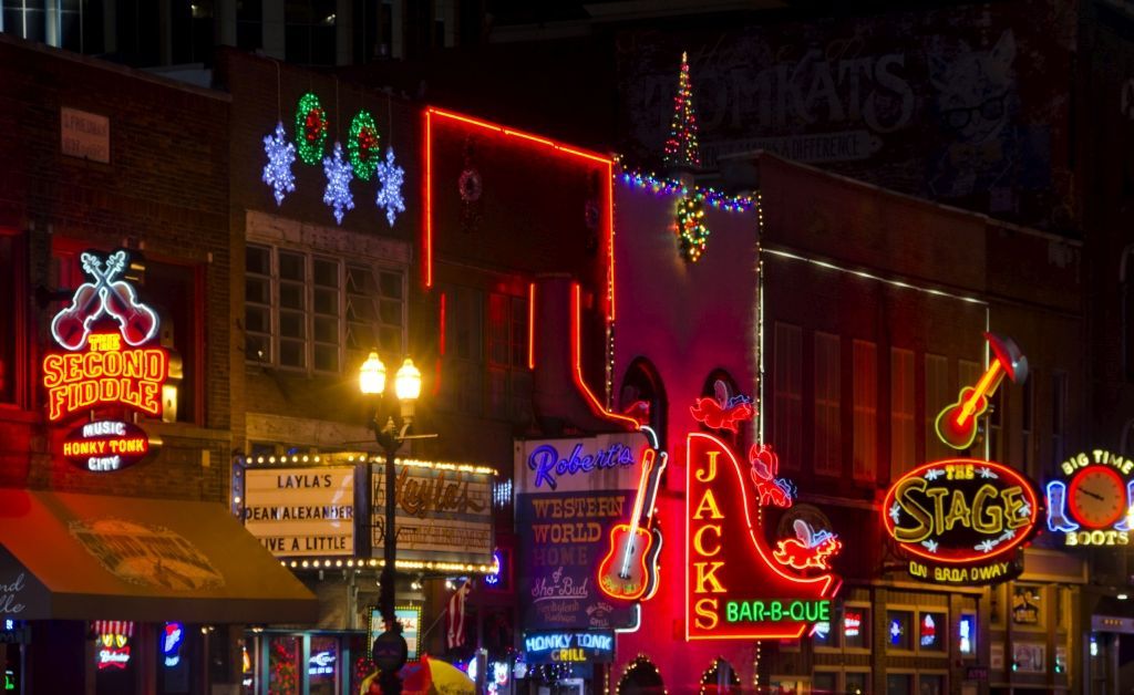 Neon signs illuminate buildings on a Nashville street at night, including Tootsie's Orchid Lounge and Robert's Western World.