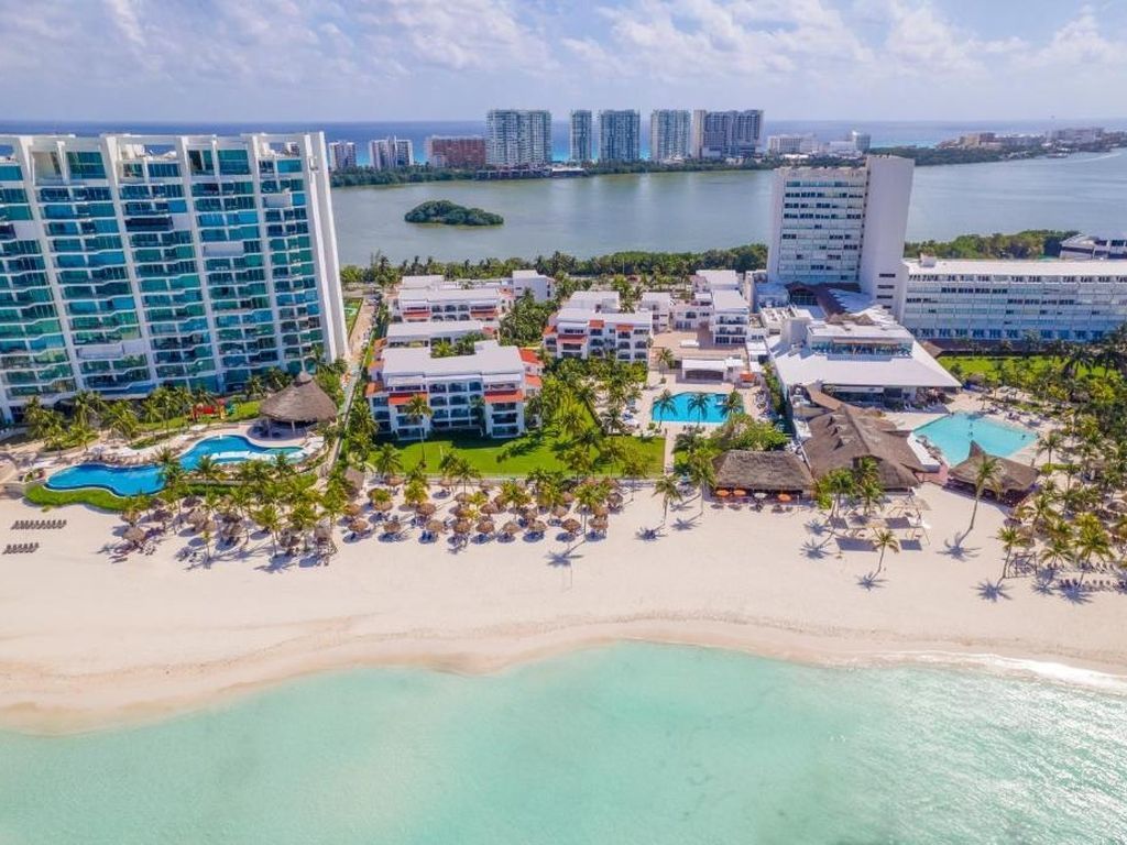 Beach resort with turquoise water, white sand, multiple pools, and tall buildings in Cancun, Mexico.