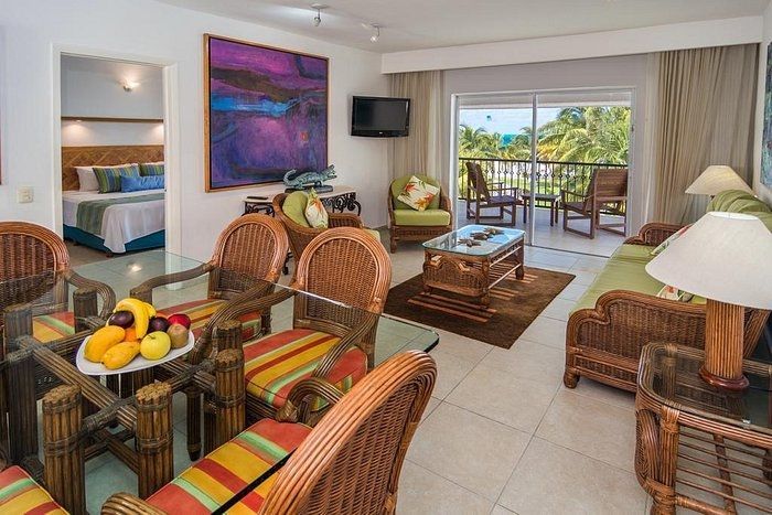 Living room with wicker furniture, balcony, and bedroom visible.