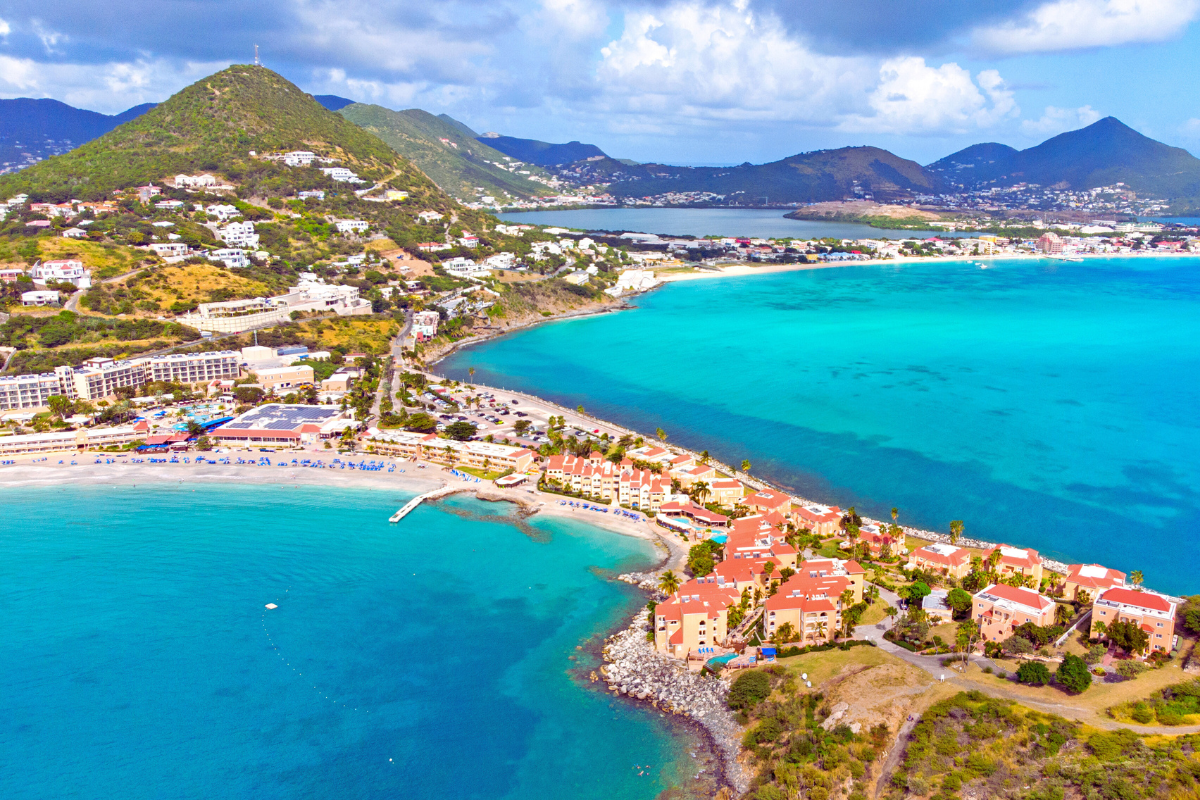 Coastal view of Simpson Bay, Saint Martin. Turquoise water, sandy beaches, and buildings with red tile roofs.