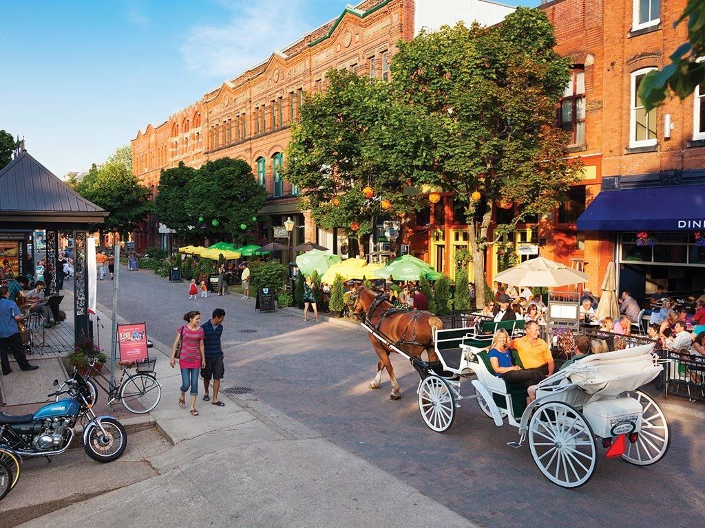 Cobblestone street scene with horse-drawn carriage, outdoor dining, and brick buildings.