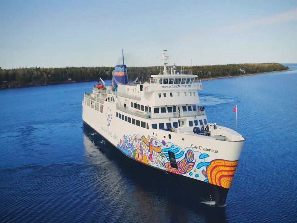 Ferry sailing on blue water, featuring colorful artwork on the hull, with a forested island in the background.
