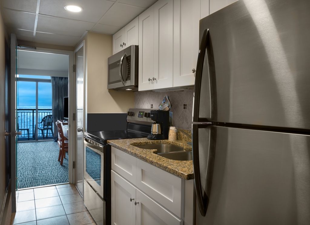 Small kitchen with white cabinets, stainless steel appliances, and view of ocean.