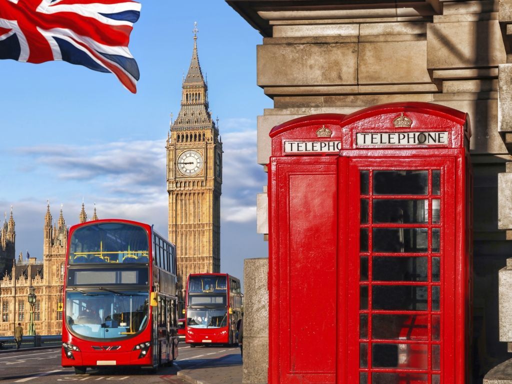 Red telephone booth, double-decker buses, and Big Ben under a British flag in London.