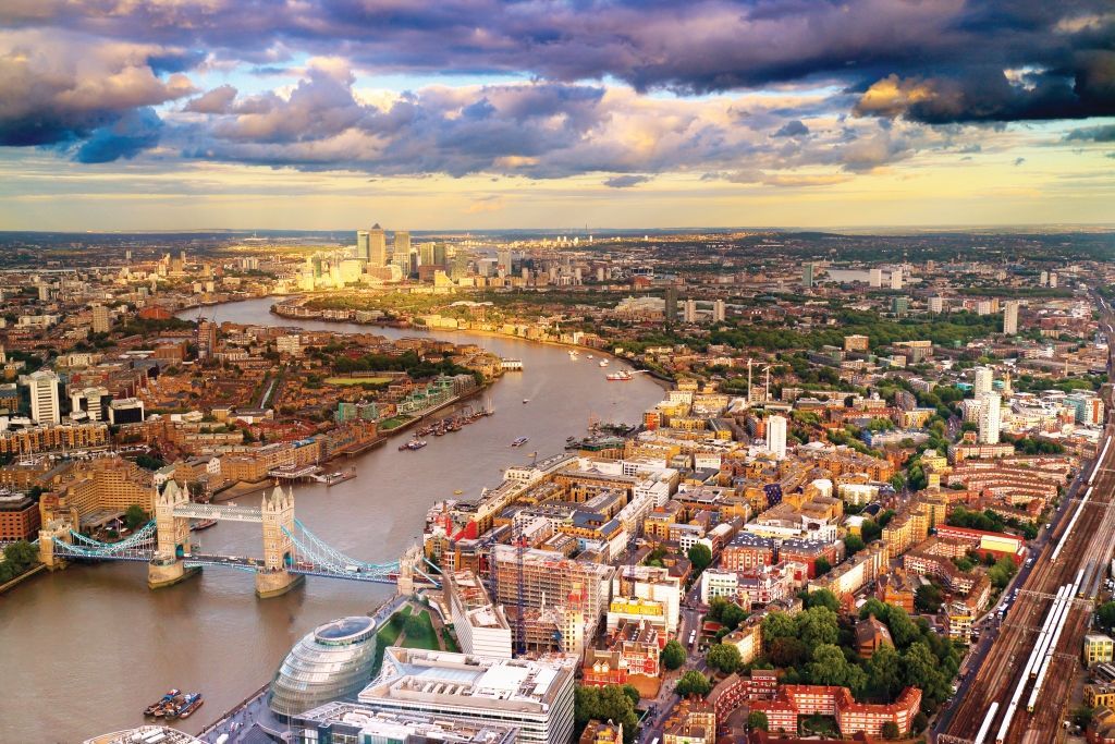 Aerial view of London, with Tower Bridge and the Thames River under a cloudy sunset sky.