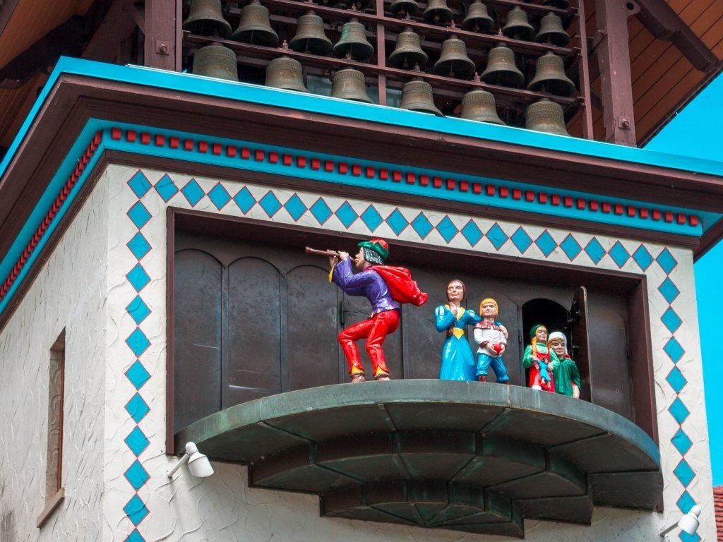 Clock tower with figures performing. Red and green-clad musician, other figurines, bronze bells above.