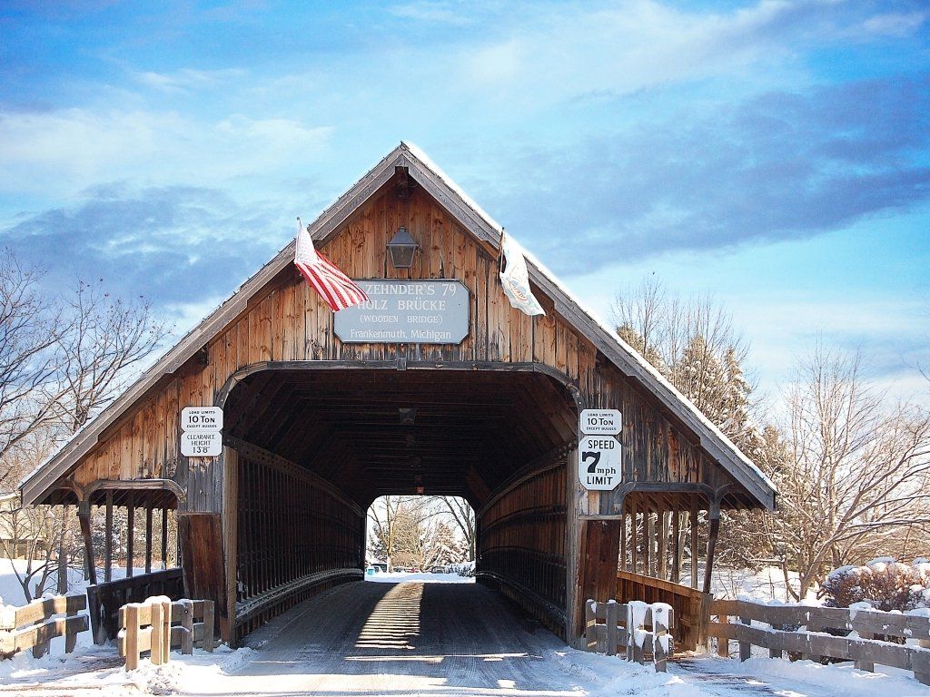 Covered wooden bridge in winter, with snow, blue sky, and American flag.
