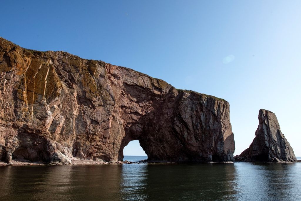 Rocky sea arch and cliff jutting into calm blue water under a clear sky
