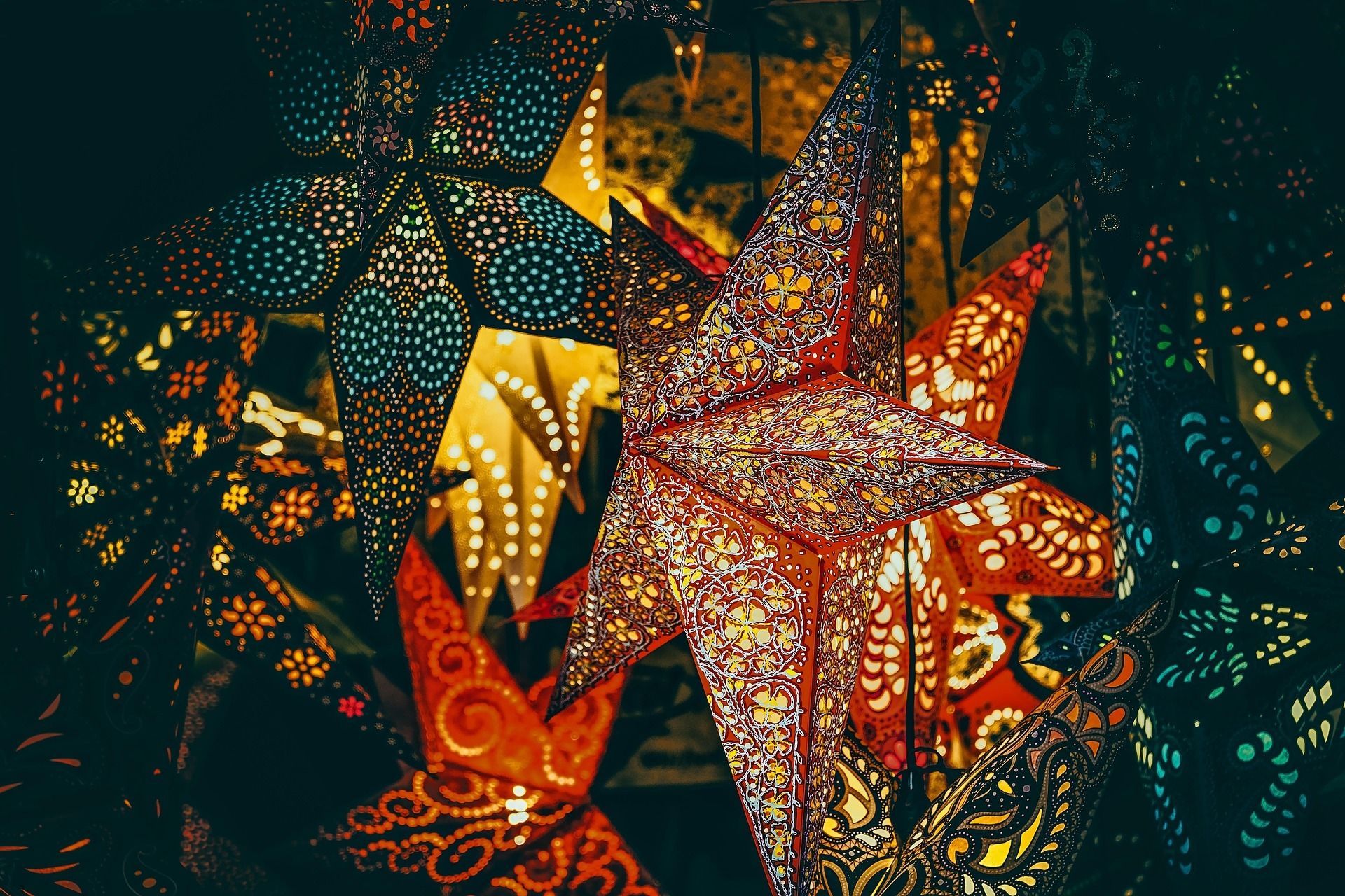 Colorful, cut-out star lanterns illuminated, creating a warm glow against a dark backdrop.