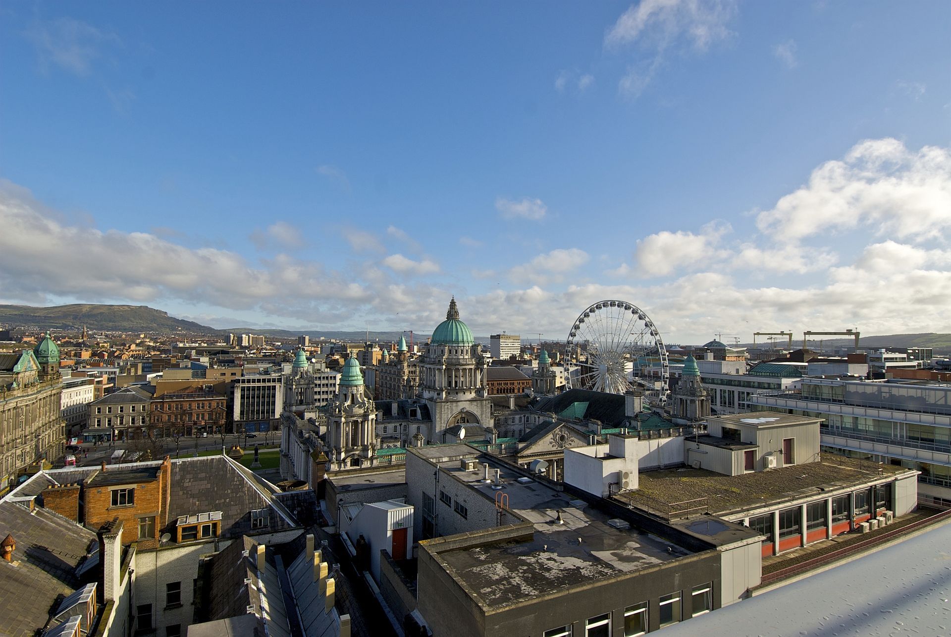 Cityscape with buildings, a Ferris wheel, and a blue sky.