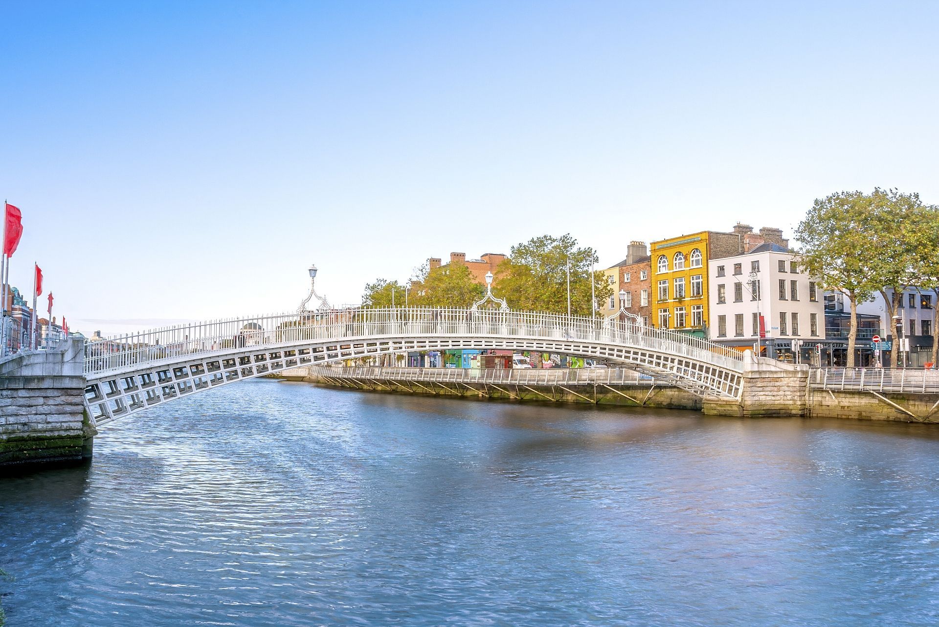 White pedestrian bridge over a river in Dublin, Ireland. Colorful buildings line the riverbank under a clear sky.