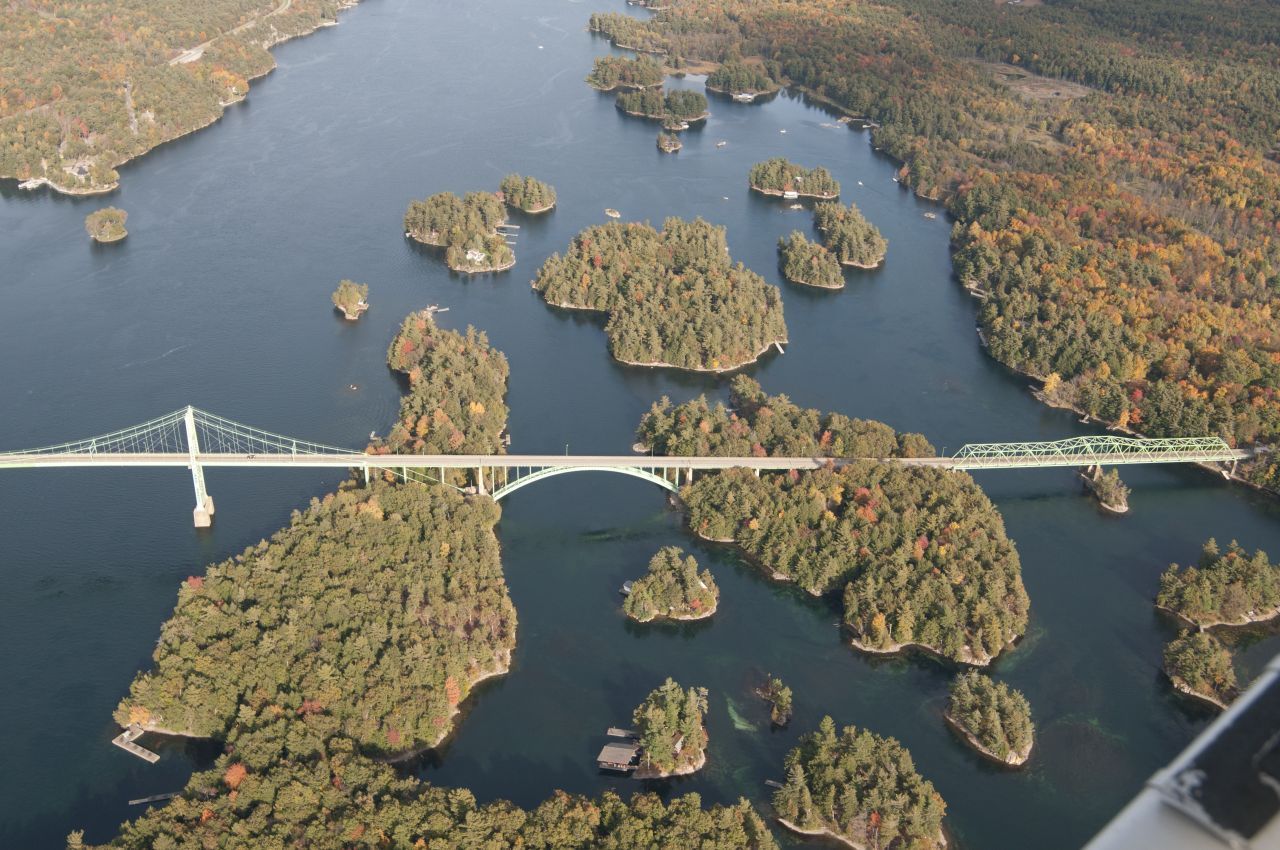 A long bridge spans a blue lake dotted with small wooded islands in autumn colors.