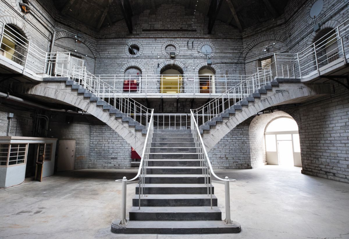 Staircase in a brick building, with two arches leading to an upper level, and an arched doorway on the right.