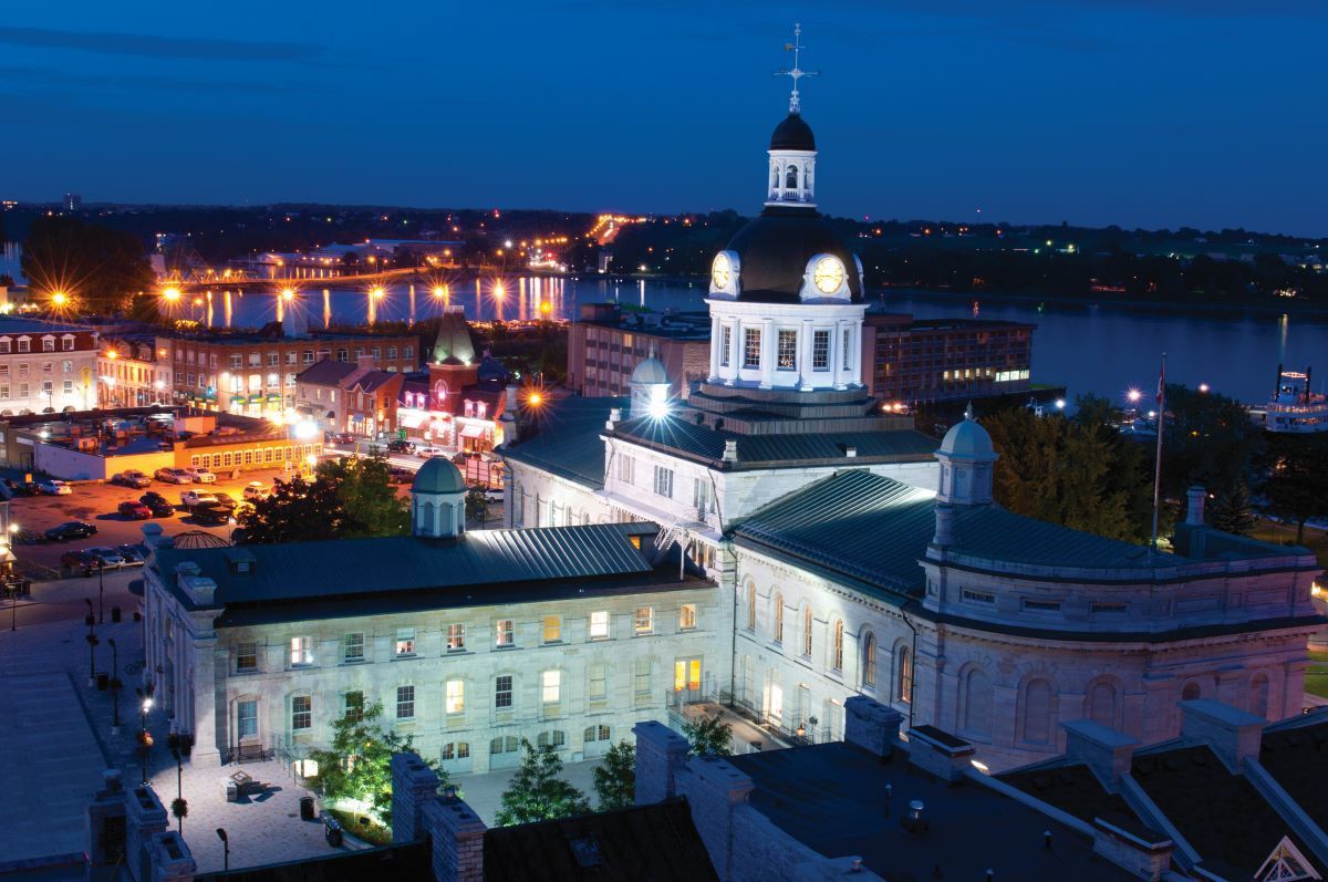 Nighttime cityscape with a lit white building and tower overlooking a waterfront harbor