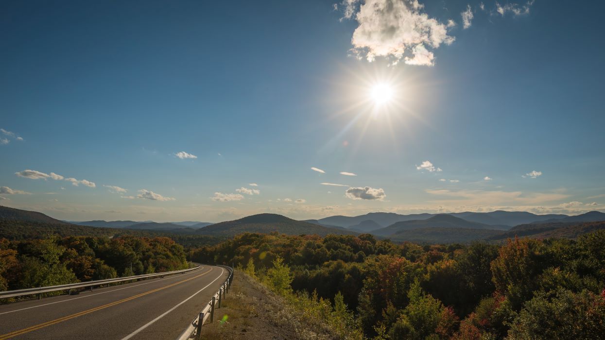 Sunlit mountain highway beside autumn trees under a clear blue sky