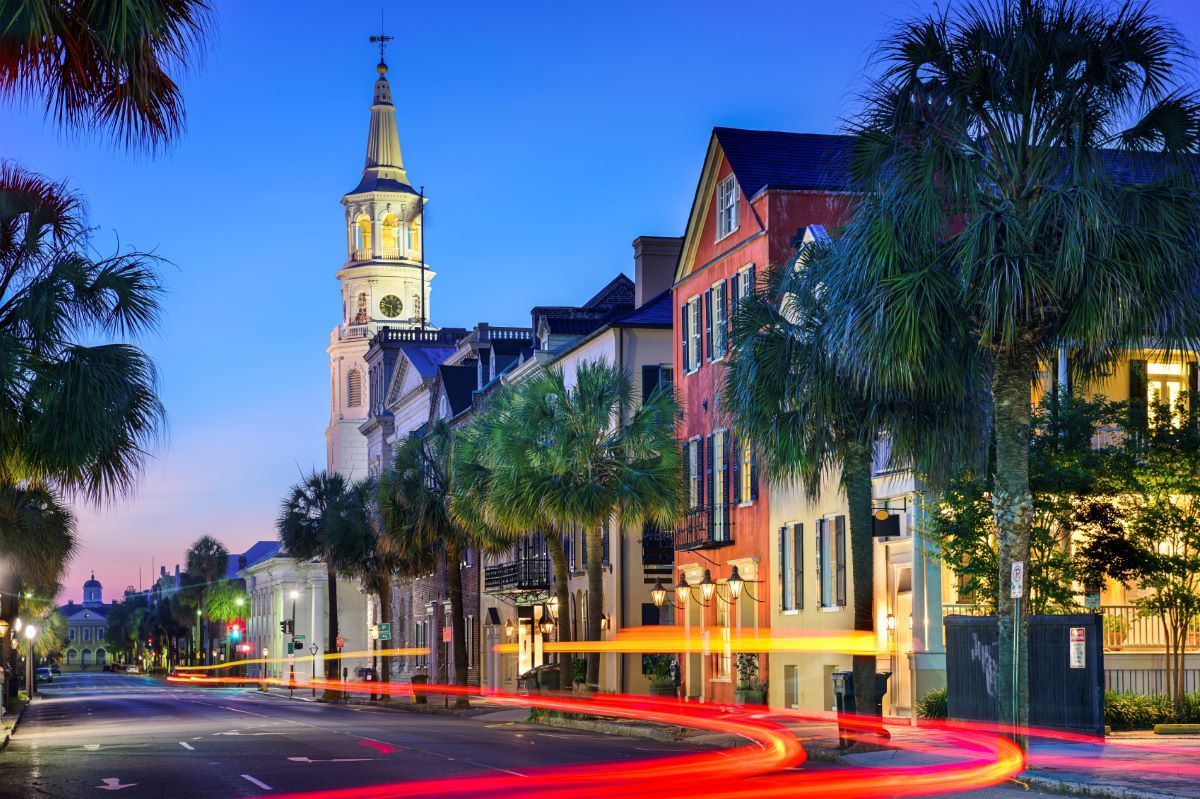 Charleston street scene at dusk with colorful buildings, a church steeple, and car light trails.