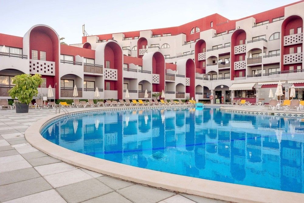 Hotel pool with blue water, surrounded by lounge chairs, and a red and white building.