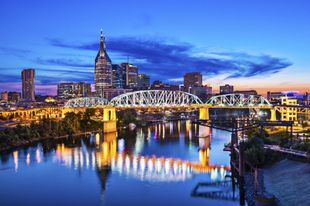 Nashville skyline with bridge over a river at dusk; city lights reflect on the water.