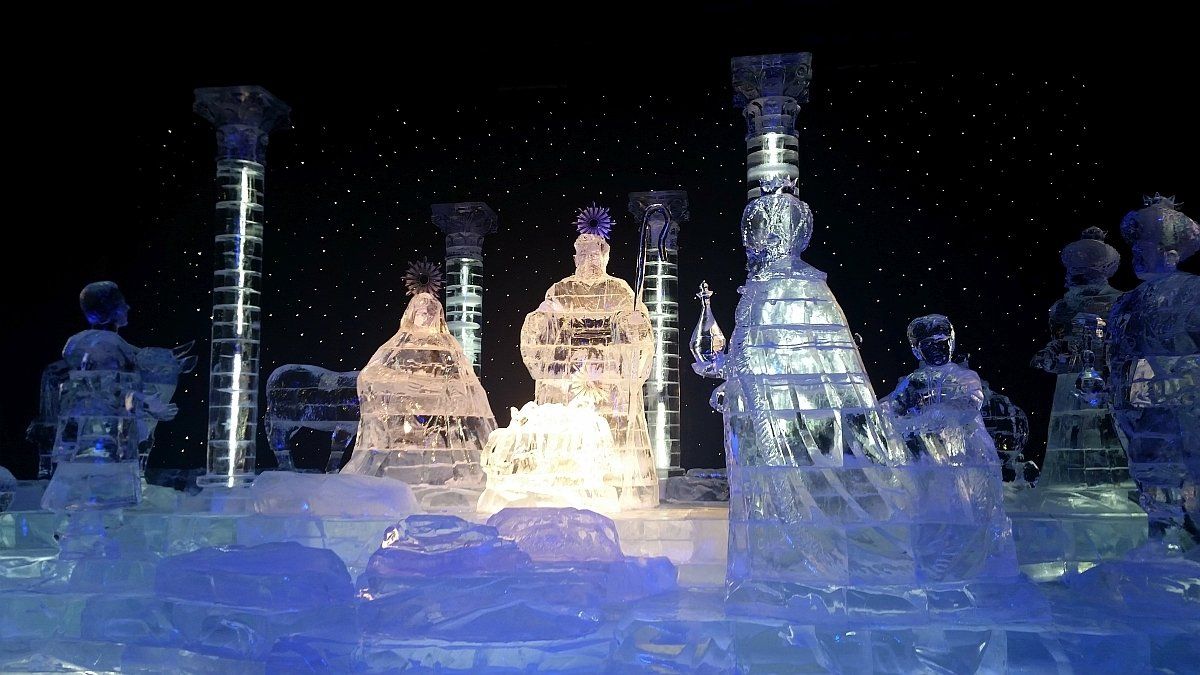 Ice sculptures of the Three Wise Men, glowing, in a Nativity scene, with columns, against a starry backdrop.