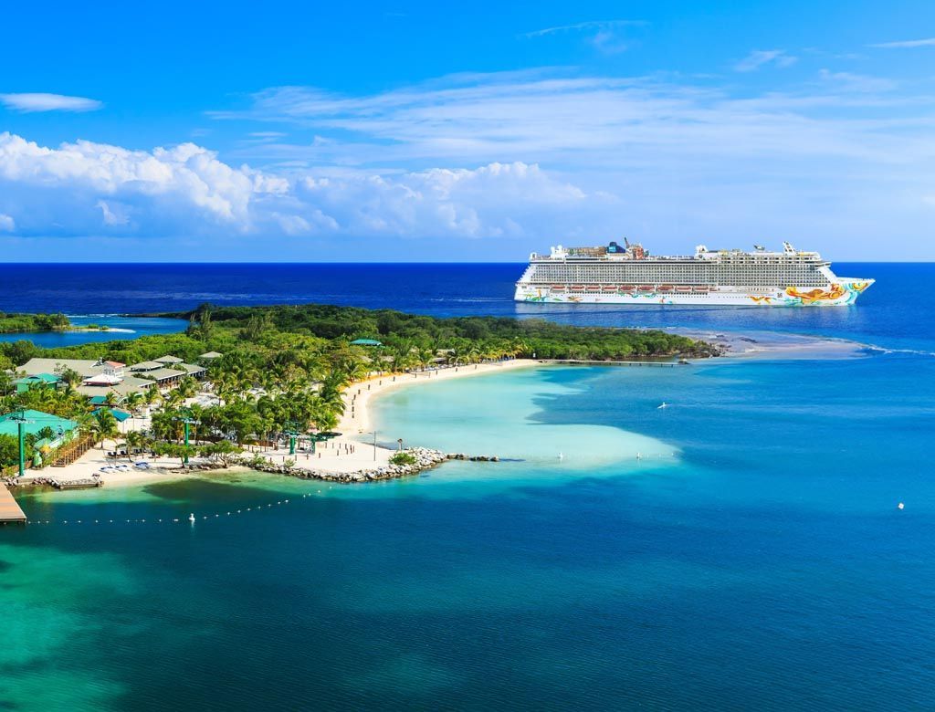 Cruise ship near tropical island with beach and blue water.