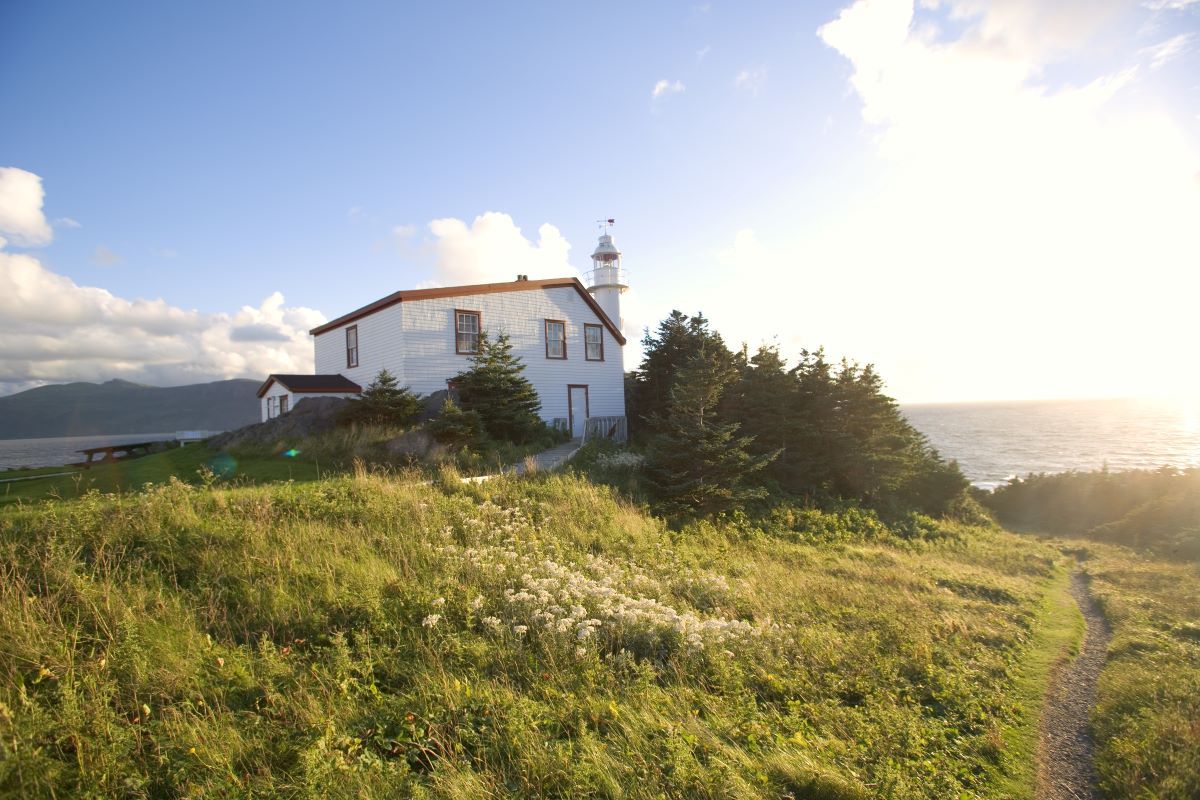 White building with a small tower on a grassy hill overlooking the ocean, sunny day.