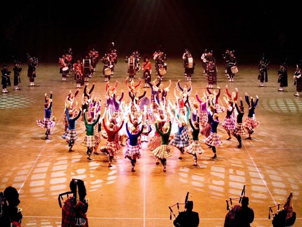 Dancers in colorful costumes perform on a lit stage in a synchronized formation.