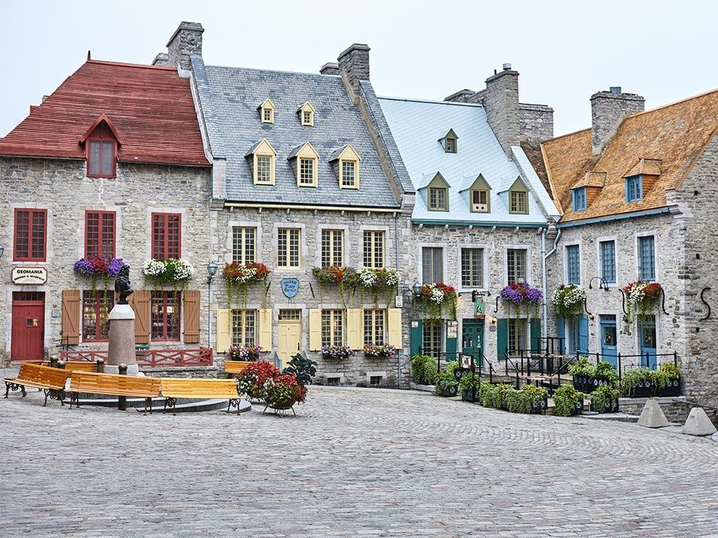 Stone buildings with colorful doors and window boxes in a cobblestone square.