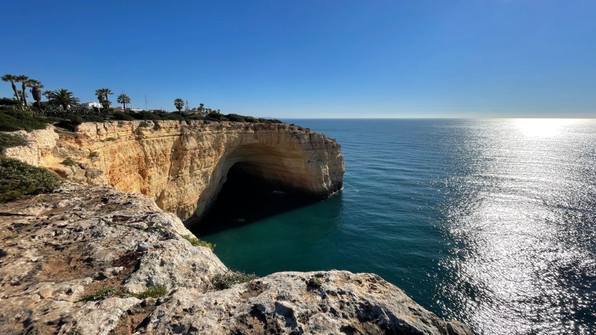 Rocky seaside cliff overlooking a turquoise cove and sunlit ocean under a clear sky