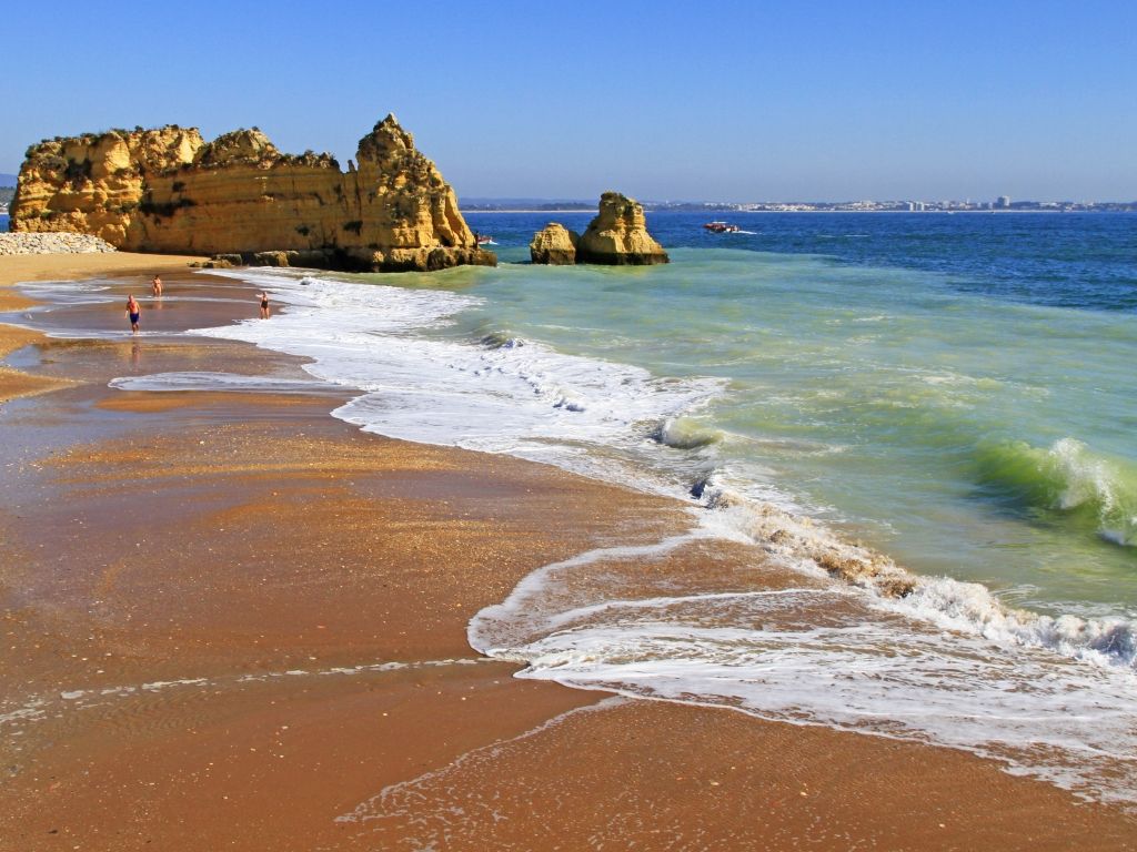 Sandy beach with golden cliffs, turquoise and blue ocean, sunny day.