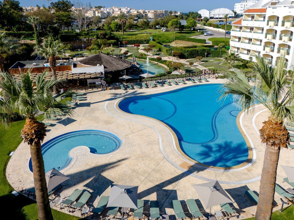 Resort pool with winding blue water, palm trees, lounge chairs, and hotel buildings in the background