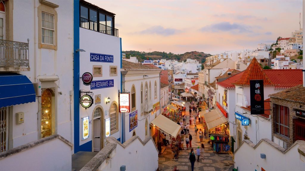 Narrow street lined with white buildings, shops, and people in a European town.