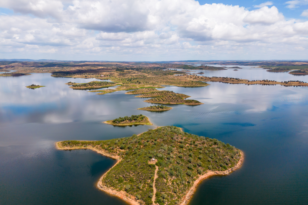 Aerial view of a lake with islands, surrounded by a landscape of trees, under a partly cloudy sky.