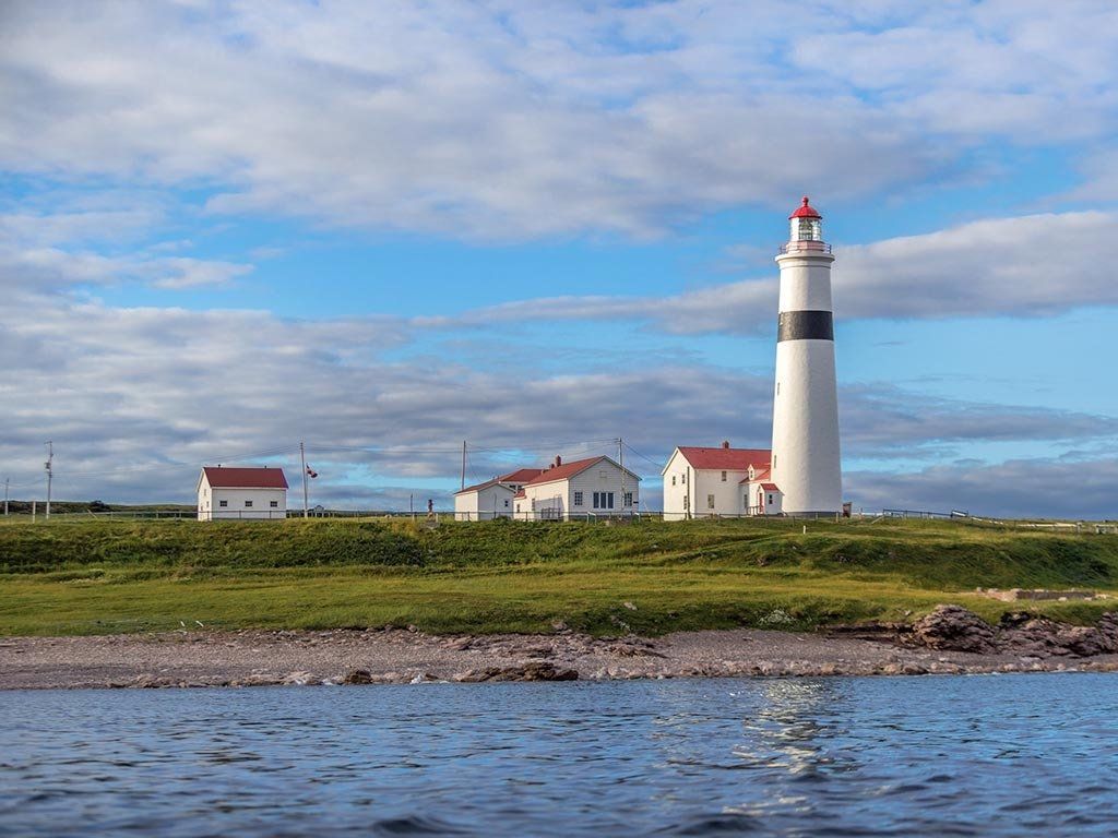 White lighthouse and seaside buildings on a grassy coast under a partly cloudy blue sky