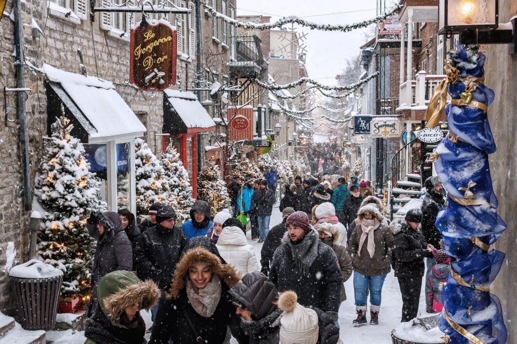 Snowy street scene in Quebec City with bundled-up tourists and Christmas decorations.