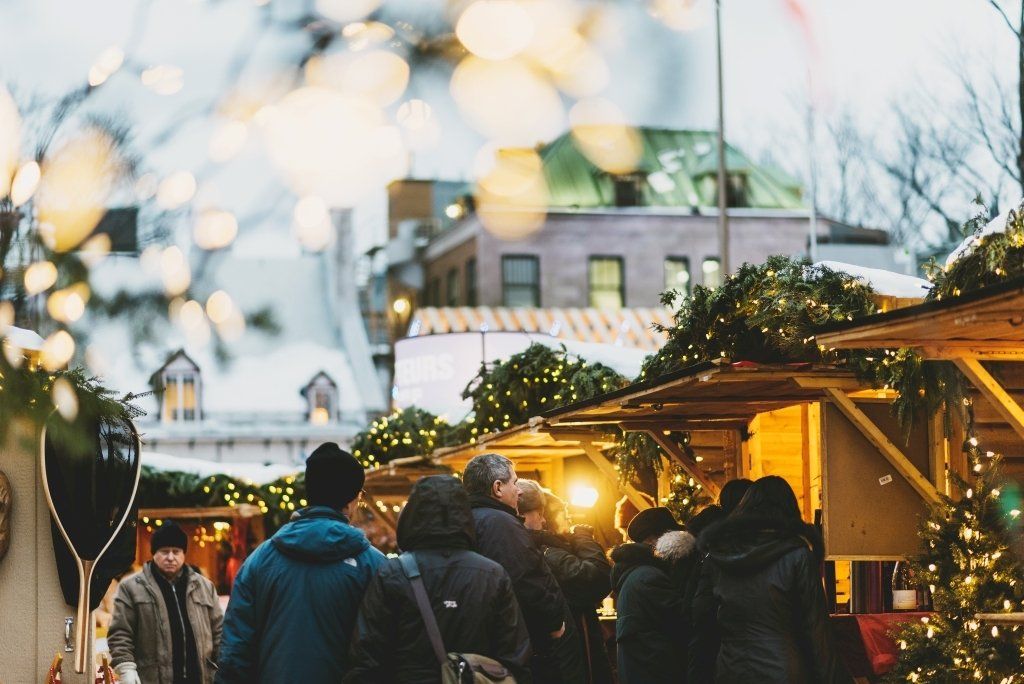 People at a Christmas market with stalls, lights, and festive decorations in winter.