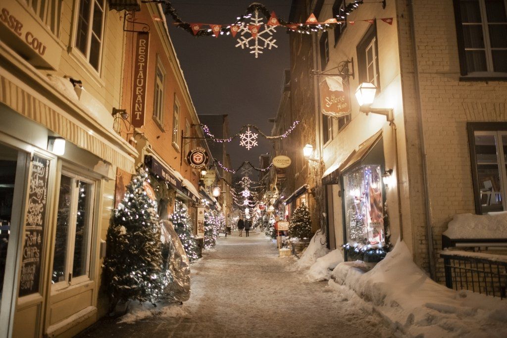 Snowy street in Quebec City at night, decorated for Christmas with lights and trees.