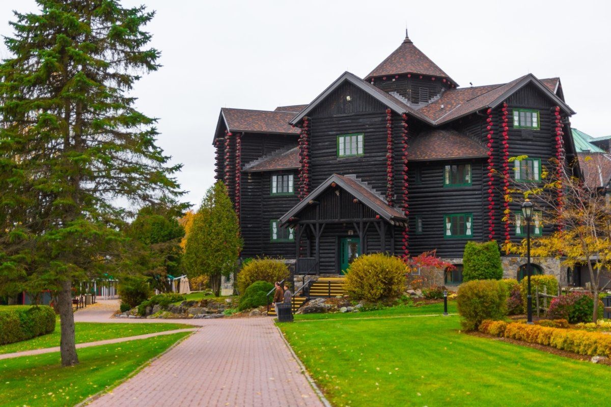 Large dark wooden lodge with a red-brick path, green lawn, and trees in front