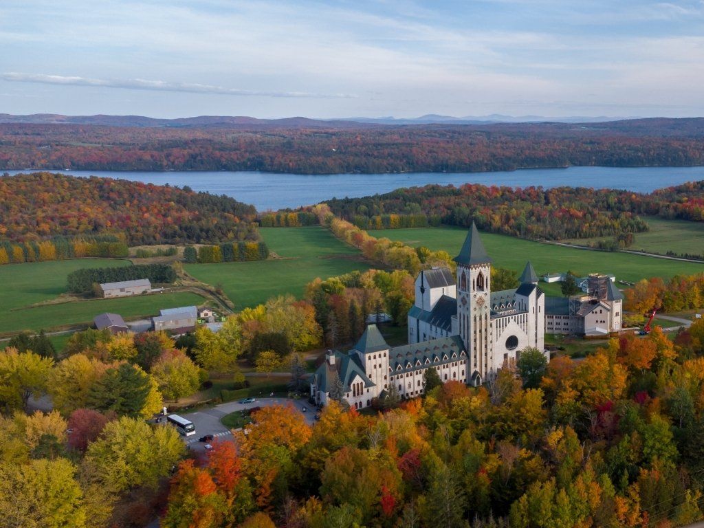 Autumn view: Abbey with tall spire, surrounded by colorful trees, field, and lake.