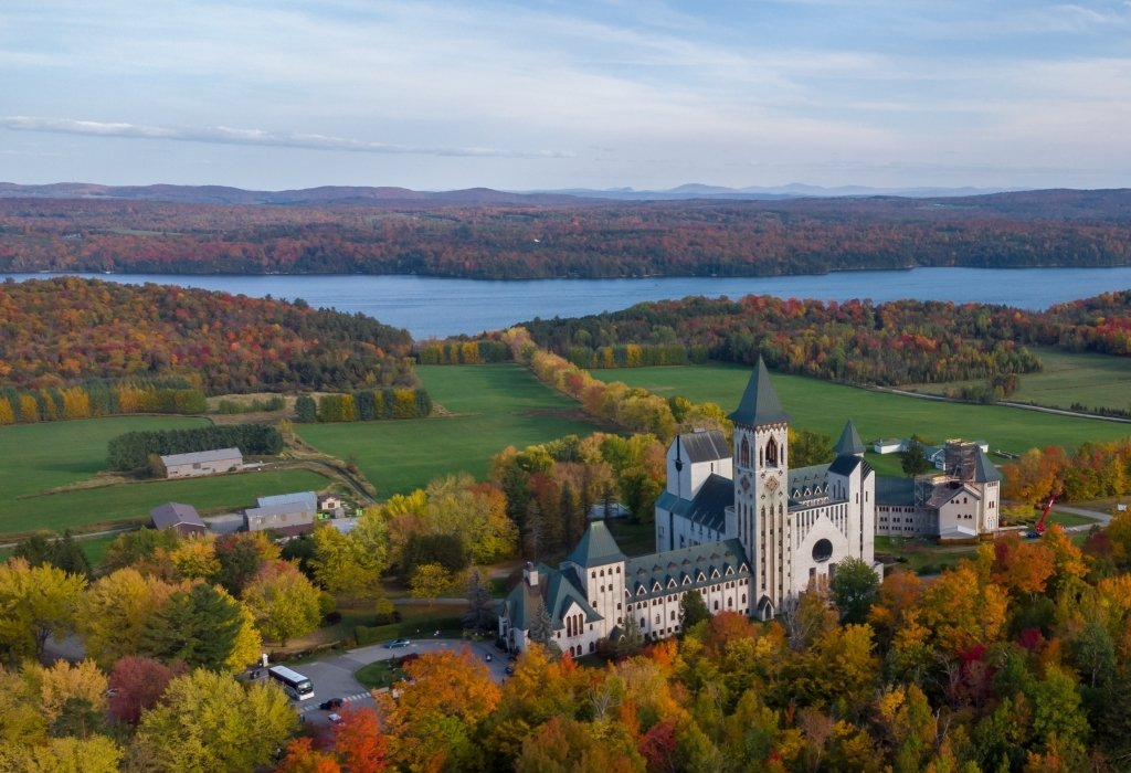 Autumn setting with a church overlooking a lake, surrounded by colourful forests and green fields