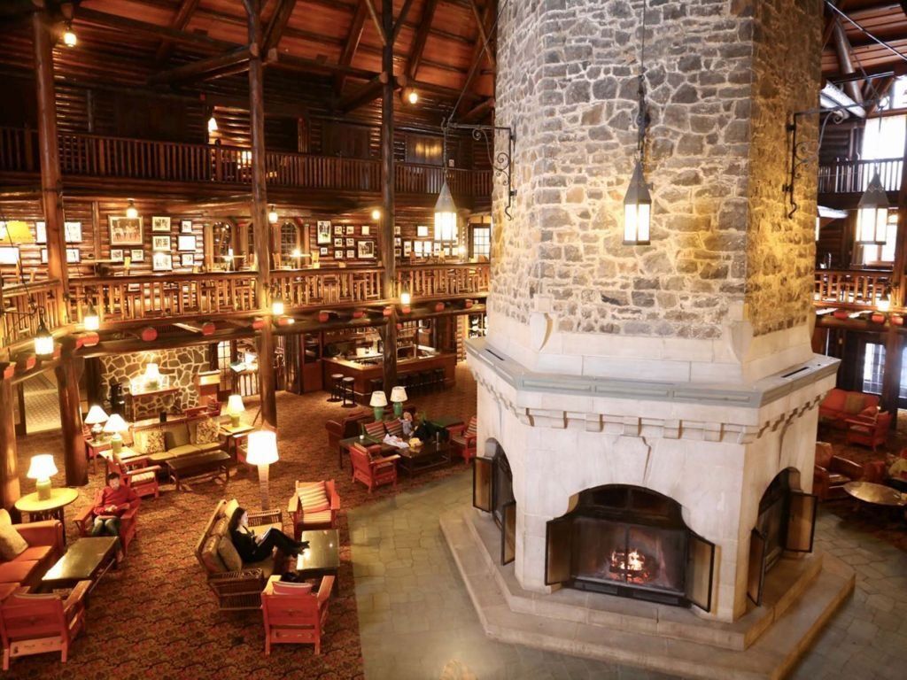 Lobby of historic lodge with a large stone fireplace and multi-level balconies, people sitting and relaxing.