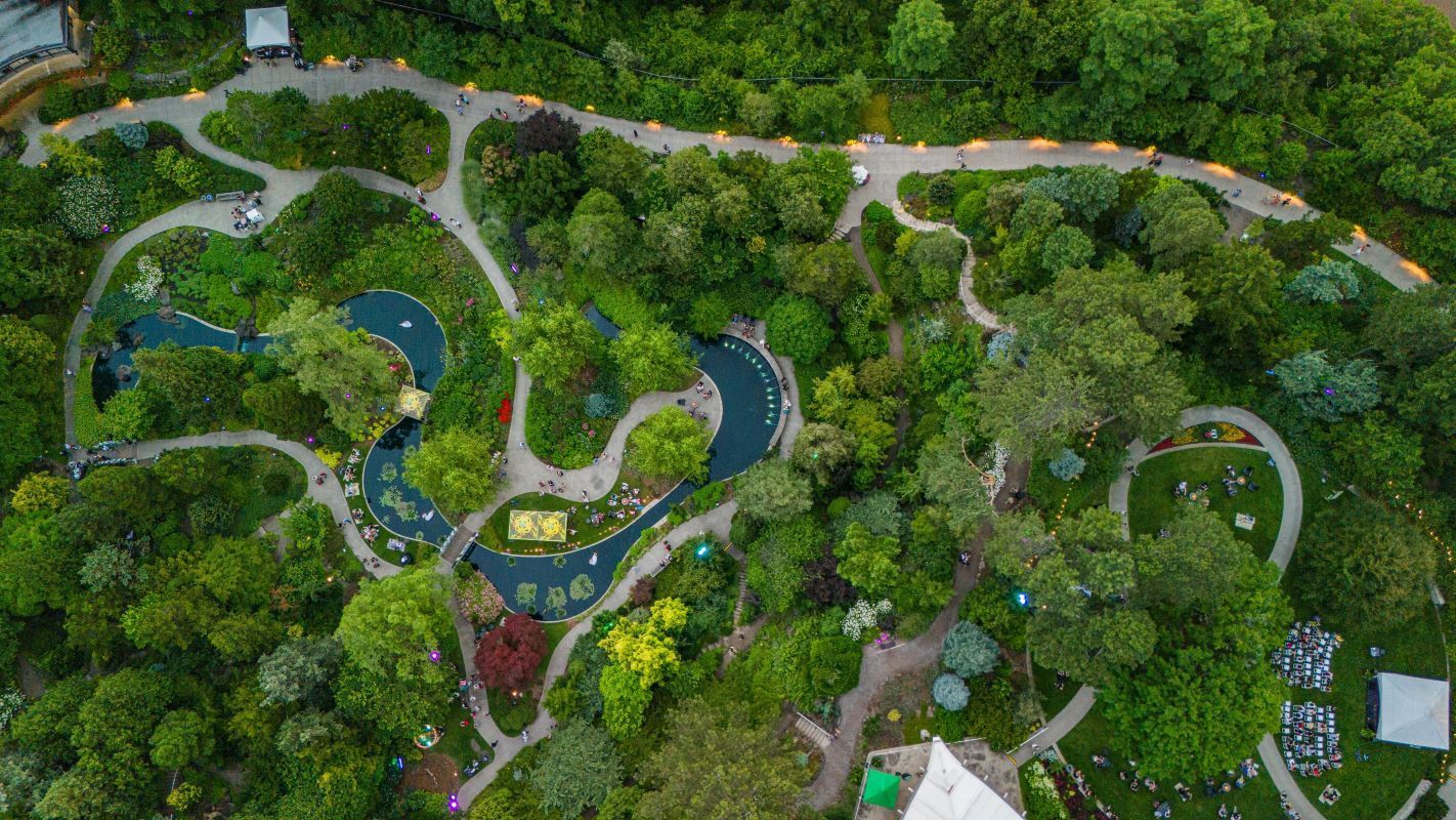 Aerial view of a lush garden maze with winding paths, ponds, and dense green trees.