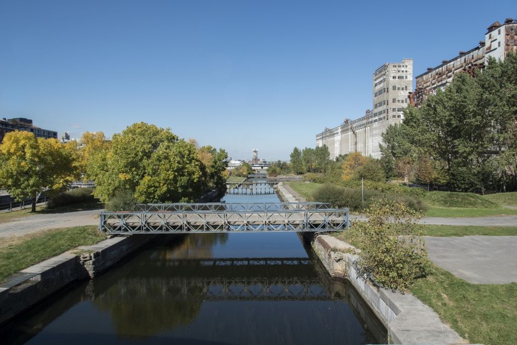 Canal with a small footbridge, trees, and buildings under a clear blue sky