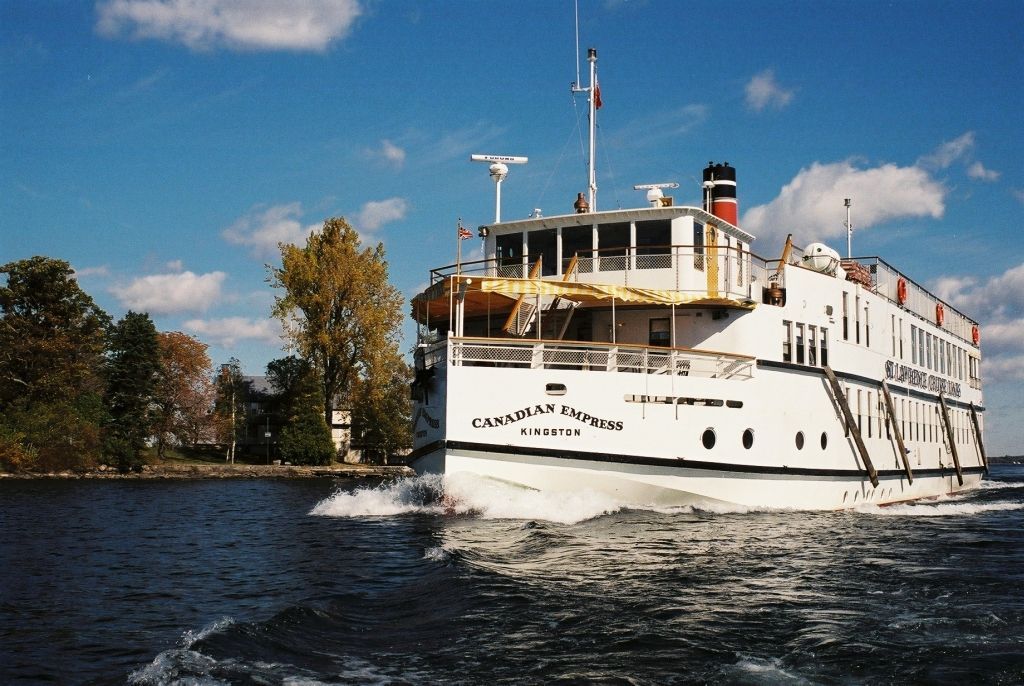 White riverboat cruising on a blue river under a partly cloudy sky, with trees on the shore.