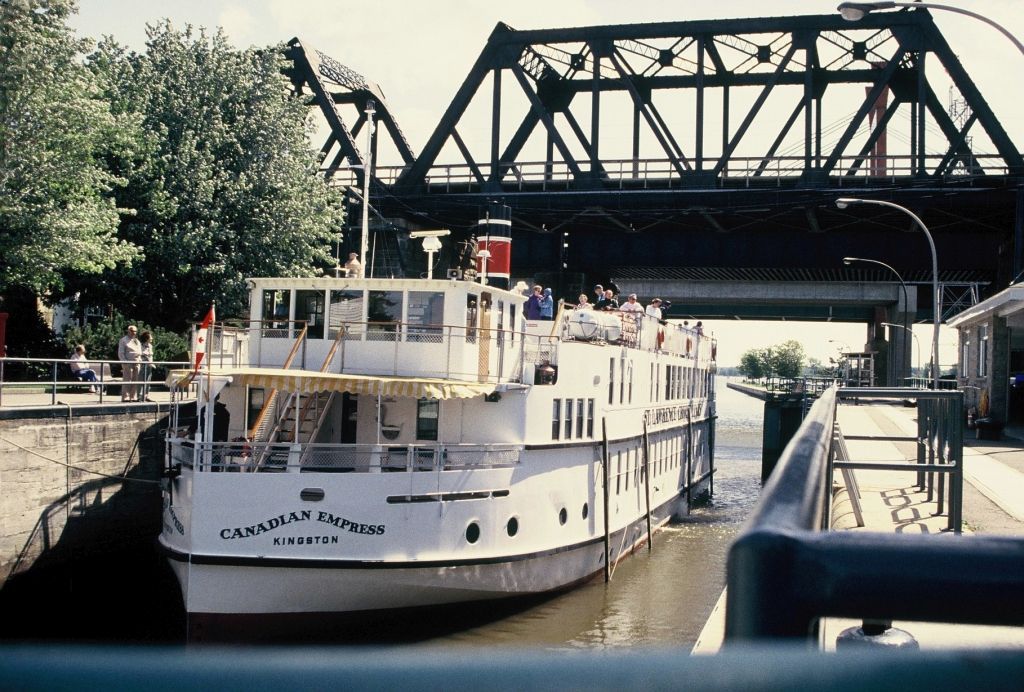 White passenger boat approaching a raised black steel bridge in a canal lock