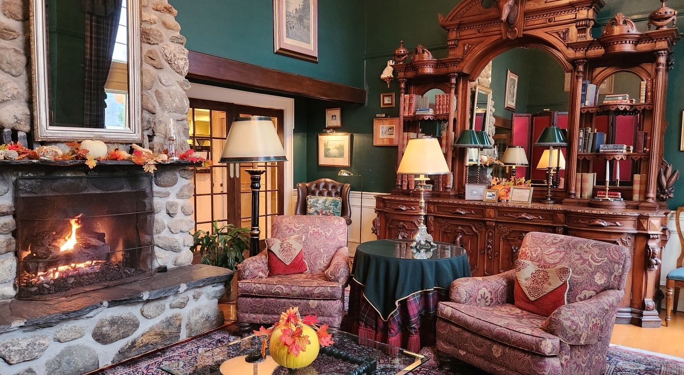 Cozy living room with fireplace, antique furniture, floral chairs, lamps, and autumn decor.