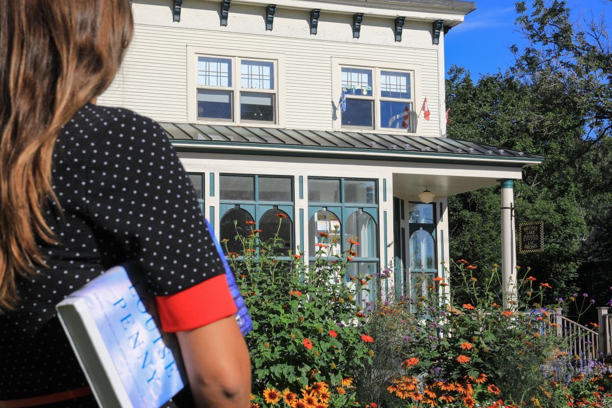Woman with a notebook looks at a white house with a porch and flower garden.